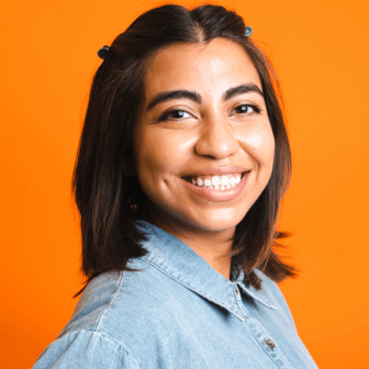 Aubrey smiling in denim shirt in front of orange background