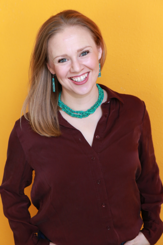 Kristen in blue shirt smiling in front of orange background